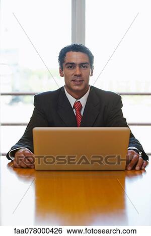 Stock Photograph - Business executive sitting at desk with laptop computer, portrait. Fotosearch