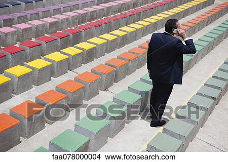 Picture - Business executive using cell phone by rows of bleachers, rear view. Fotosearch