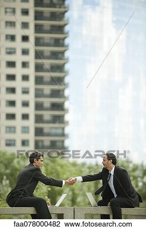 Business executives sitting outdoors with laptop computers, shaking hands View Large Photo Image Stock Image - Business executives sitting outdoors with laptop computers, shaking hands. Fotosearch