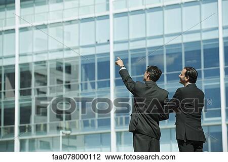 Stock Image - Business executives standing in front of office building, one pointing into distance. Fotosearch