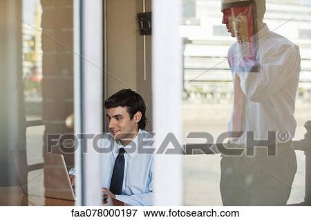 Stock Photo - Businessman in office seen from outside of window, reflection of man using cell phone outdoors. Fotosearch