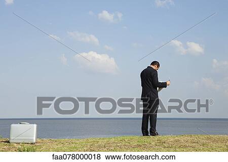 Businessman reading newspaper by ocean, rear view View Large Photo Image Stock Photo - Businessman reading newspaper by ocean, rear view. Fotosearch