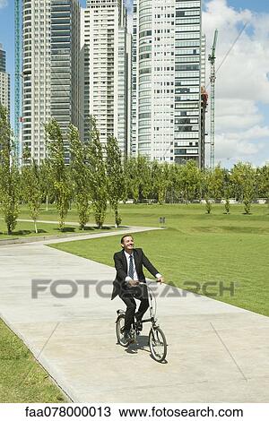 Stock Image - Businessman riding bicycle in park. Fotosearch