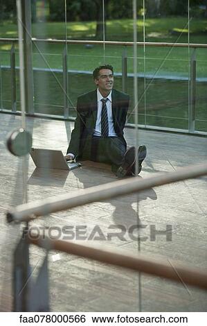 Stock Photograph - Businessman sitting on deck outdoors with laptop computer. Fotosearch