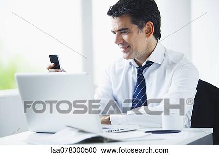 Stock Image - Businessman using cell phone at work. Fotosearch
