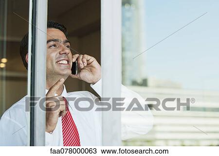 Businessman using cell phone in office, seen from outside of window View Large Photo Image Stock Image - Businessman using cell phone in office, seen from outside of window. Fotosearch