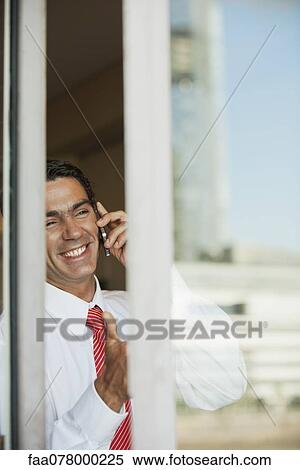 Stock Photography - Businessman using cell phone in office, seen from outside of window. Fotosearch
