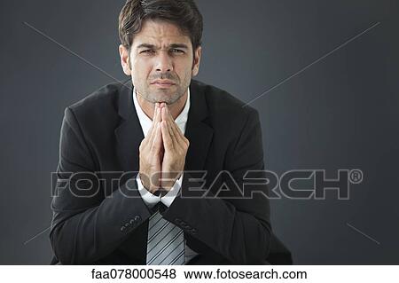 Stock Photo - Businessman with hands clasped under chin, disappointed expression on face. Fotosearch