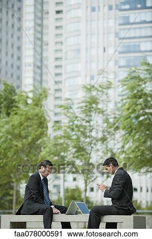 Businessmen sitting outdoors with laptop computers, one man text messaging with cell phone View Large Photo Image Stock Image - Businessmen sitting outdoors with laptop computers, one man text messaging with cell phone. Fotosearch