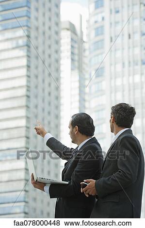 Stock Photo - Businessmen using laptop computer outdoors, one man pointing into distance. Fotosearch