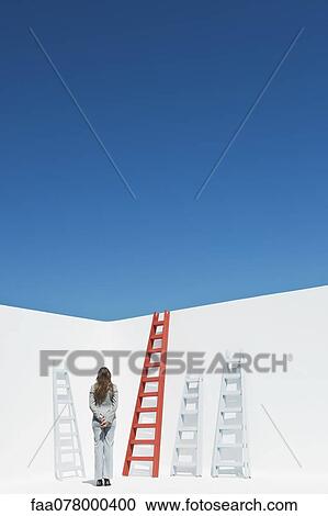Stock Image - Businesswoman contemplating ladders, rear view. Fotosearch