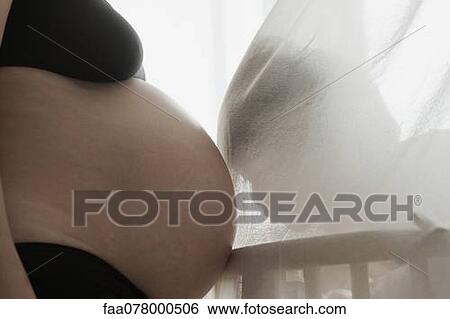 Stock Photograph - Child behind curtain, resting head on mother's pregnant belly, backlit. Fotosearch