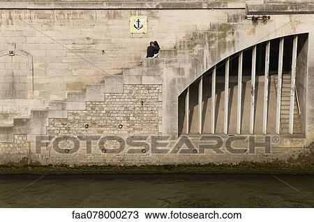 Stock Image - Couple embracing on steps by river. Fotosearch