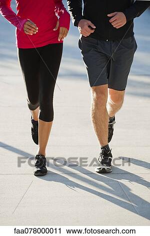 Stock Image - Couple jogging side by side, low section. Fotosearch