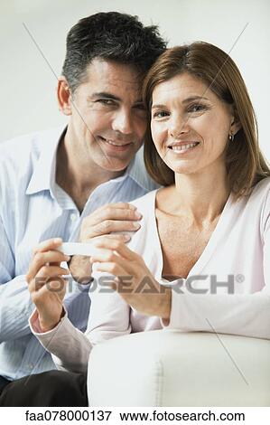 Stock Photo - Couple smiling, woman holding pregnancy test. Fotosearch