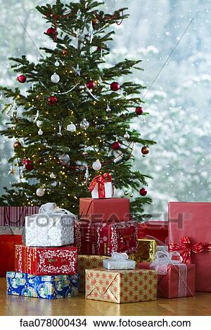 Festively wrapped gifts stacked in front of Christmas tree View Large Photo Image Picture - Festively wrapped gifts stacked in front of Christmas tree. Fotosearch