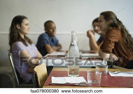 Stock Image - Friends hanging out in cafe, focus on empty table in foreground. Fotosearch