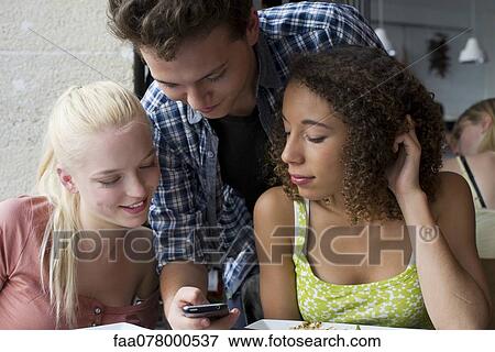 Stock Photo - Friends looking at cell phone together. Fotosearch