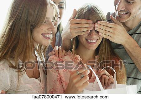 Friends watching young woman opening gift View Large Photo Image Stock Image - Friends watching young woman opening gift. Fotosearch