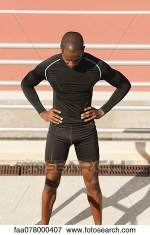 Stock Photo - Male athlete standing by running track with head down. Fotosearch
