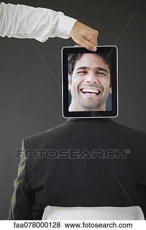 Stock Photo - Man concealed behind digital tablet displaying image of laughing man, rear view. Fotosearch