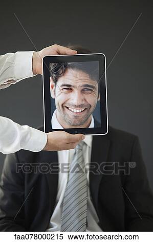 Stock Photography - Man concealed behind digital tablet displaying image of smiling man. Fotosearch