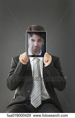 Stock Photo - Man holding frowning photograph in front of his face. Fotosearch