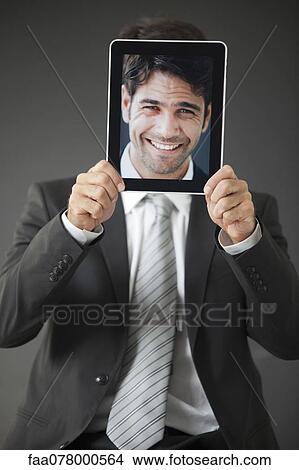 Picture - Man holding smiling photograph in front of his face. Fotosearch