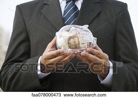 Stock Image - Man holding transparent piggy bank filled with euros, cropped. Fotosearch