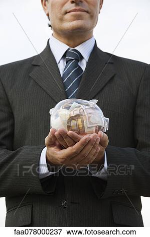 Man holding transparent piggy bank filled with euros View Large Photo Image Stock Photo - Man holding transparent piggy bank filled with euros. Fotosearch