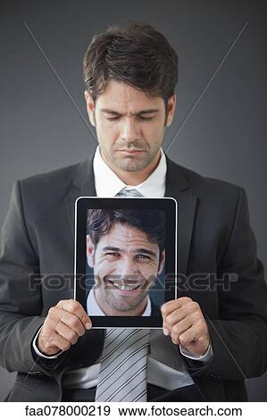 Stock Photo - Man holding up digital tablet displaying image of himself smiling. Fotosearch
