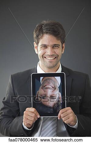 Stock Photography - Man holding up digital tablet displaying upside down image of himself smiling. Fotosearch