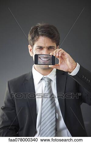 Man holding up smartphone displaying image of his own smile View Large Photo Image Stock Image - Man holding up smartphone displaying image of his own smile. Fotosearch