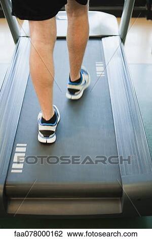 Stock Image - Man running on treadmill, low section, rear view. Fotosearch