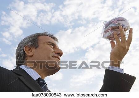 Mature man holding up transparent piggy bank filled with euros View Large Photo Image Stock Image - Mature man holding up transparent piggy bank filled with euros. Fotosearch