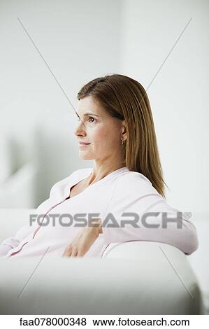 Stock Photo - Mature woman sitting on couch, side view. Fotosearch