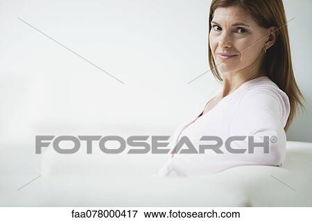 Mature woman sitting on couch, smiling over shoulder View Large Photo Image Stock Photo - Mature woman sitting on couch, smiling over shoulder. Fotosearch