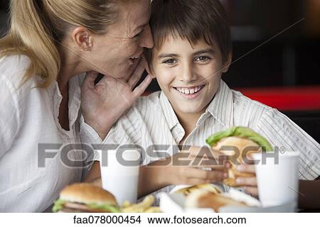 Picture - Mother whispering in son's ear in fast food restaurant. Fotosearch
