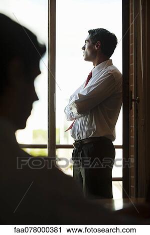 Stock Image - Silhouette of businessman standing by window. Fotosearch