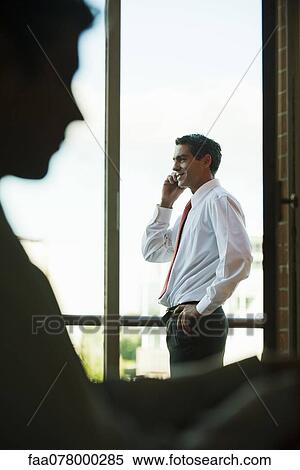 Stock Photography - Silhouette of businessman using cell phone by window. Fotosearch