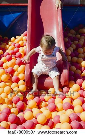 Stock Photo - Toddler girl going down slide into ball pit on playground. Fotosearch