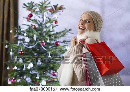 Woman carrying shopping bags, Christmas tree in background View Large Photo Image Stock Photo - Woman carrying shopping bags, Christmas tree in background. Fotosearch