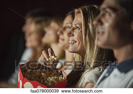 Stock Photo - Woman eating popcorn while watching movie in theater. Fotosearch
