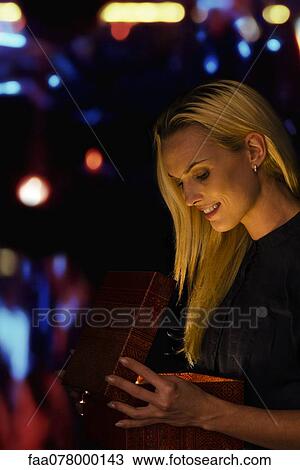 Woman illuminated by golden light as she opens Christmas gift View Large Photo Image Stock Image - Woman illuminated by golden light as she opens Christmas gift. Fotosearch