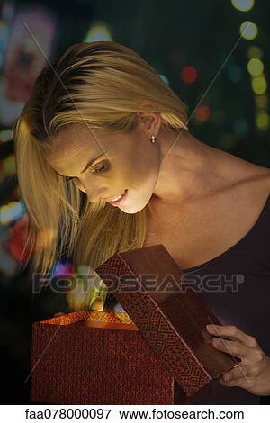 Woman illuminated by golden light as she opens Christmas gift View Large Photo Image Stock Photo - Woman illuminated by golden light as she opens Christmas gift. Fotosearch
