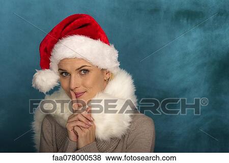 Stock Photo - Woman wearing Santa hat, finger on lips, portrait. Fotosearch