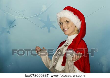 Stock Photo - Woman wearing Santa hat in front of festive background, portrait. Fotosearch