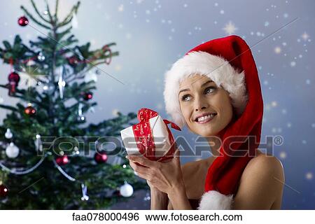 Stock Photograph - Woman wearing Santa hat, shaking Christmas gift. Fotosearch