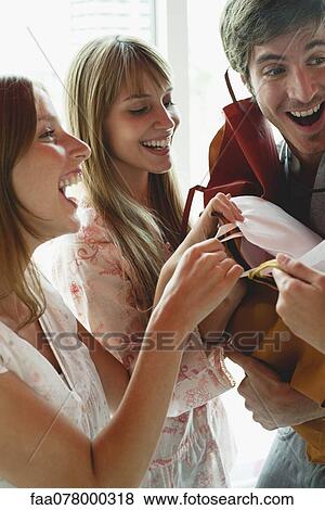Stock Photo - Women grabbing gift bags in man's arms. Fotosearch