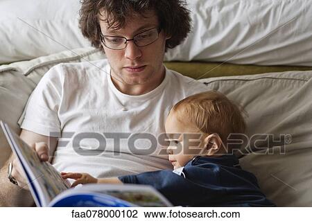 Stock Image - Young man reading book to baby boy. Fotosearch